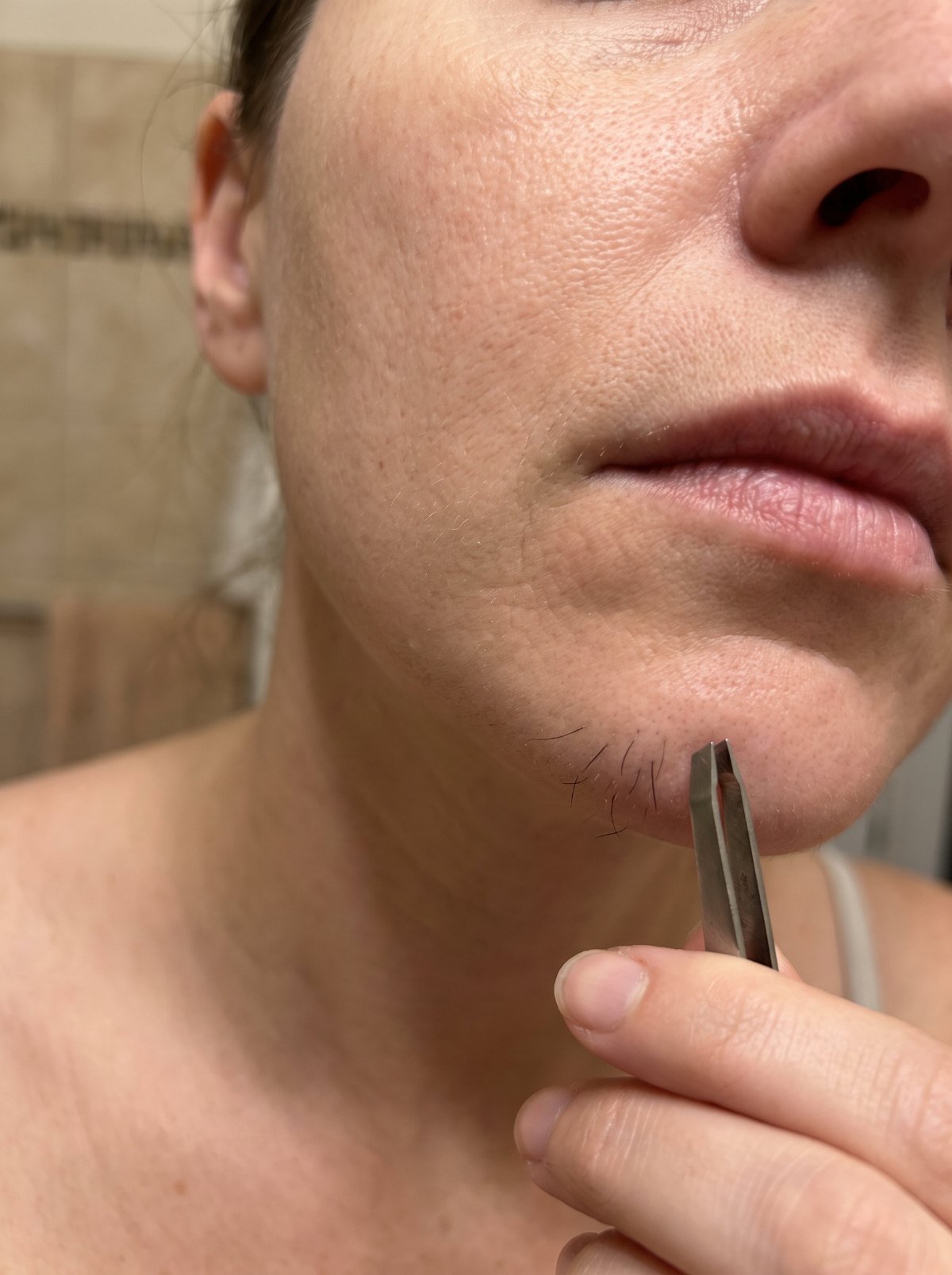 Woman holding tweezers near dark chin hairs